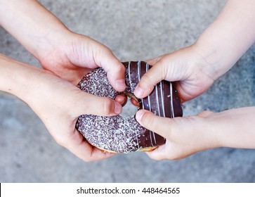 Children's Hands Holding A Chocolate Donut. Two Kids Pull To Themselves Donut. Closeup.the Concept Of Sharing Food