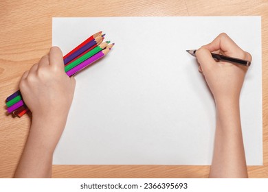 Children's hands on the table, white sheet of paper and colored pencils, concept of children's creativity. Child's hand with a blank sheet of paper and different pencils. Empty space for your text - Powered by Shutterstock