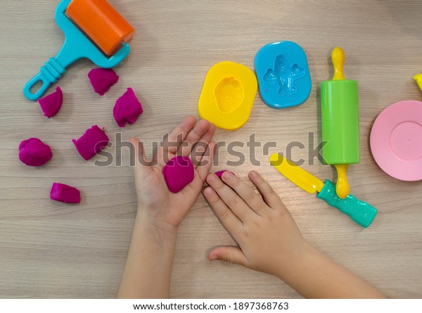 Children\'s hands play with colored clay. The\
child plays at home and creates flower from plasticine. She sculpts\
clay stucco.