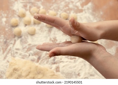Las manos de los niños rompen una bola de masa entre las palmas con el fondo de bolas de masa ya hechas, un gran trozo de masa y una mesa de madera con harina. El proceso de elaboración del postre