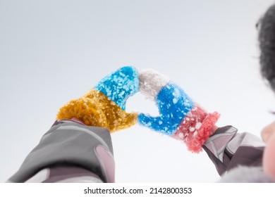 Children's Hands In Snow-covered Mittens Are Folded In The Shape Of A Heart, One Mitten Is In The Colors Of The Flag Of Ukraine, And The Other Is In The Colors Of The Flag Of Russia