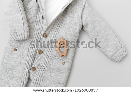 Children's knitted jumpsuit and wooden teething toy hedgehog on a gray background. Baby clothes, flat lay.