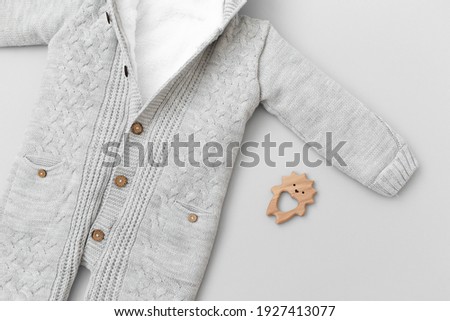 Children's knitted jumpsuit and wooden teething toy hedgehog on a gray background. Baby clothes, flat lay.