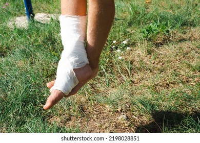 Children's Legs Are Bandaged In Plaster - Barefoot On A Swing. Traumatic Equipment, Child Injury, Bruise, Sprain, Fracture