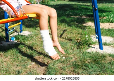 Children's Legs Are Bandaged In Plaster - Barefoot On A Swing. Traumatic Equipment, Child Injury, Bruise, Sprain, Fracture