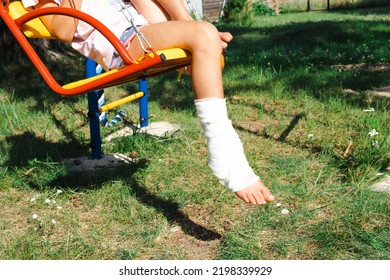 Children's Legs Are Bandaged In Plaster - Barefoot On A Swing. Traumatic Equipment, Child Injury, Bruise, Sprain, Fracture