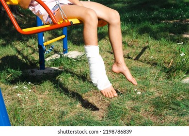 Children's Legs Are Bandaged In Plaster - Barefoot On A Swing. Traumatic Equipment, Child Injury, Bruise, Sprain, Fracture