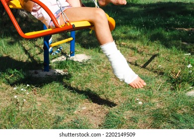 Children's Legs Are Bandaged In Plaster - Barefoot On A Swing. Traumatic Equipment, Child Injury, Bruise, Sprain, Fracture