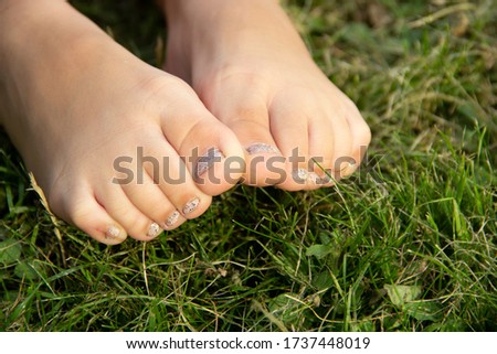 Children's legs close-up with manicure on a background of green grass