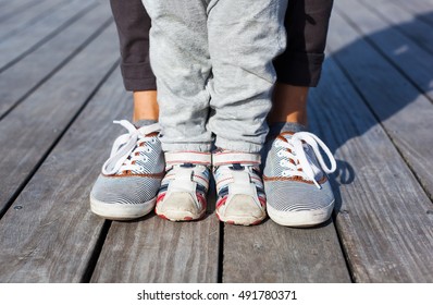 Children's legs and feet in shoes adult sneakers with each other on wooden background. Family background. Lifestyle and Travel concept. Parent and child together.
