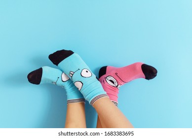 Children's Legs In Funny Socks Raised Up On A Blue Background, Feet Having Fun, Creative Concept