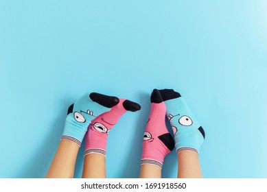 Children's Legs In Funny Socks Raised Up On A Blue Background, Feet Having Fun, Creative Concept