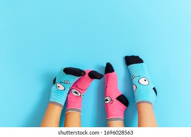 Children's Legs In Funny Socks Raised Up On A Blue Background, Feet Having Fun, Creative Concept