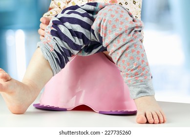Children's legs hanging down from a chamber-pot on a blue  background