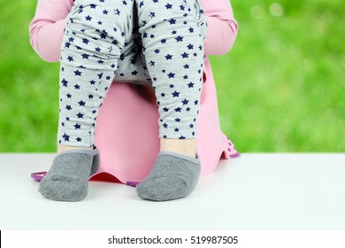 Children's legs hanging down from a chamber-pot on a green background