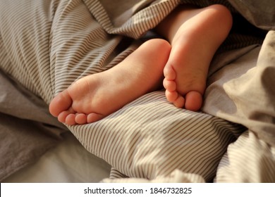 Children's Legs Stick Out From Under The Warm Blanket. Concept Of Care, Proper Sleep, And Home Comfort.