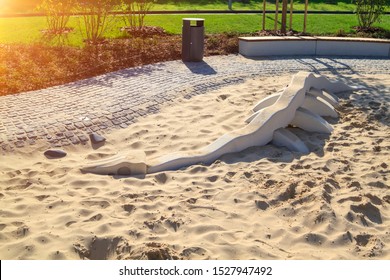 childrens modern playground with sandbox in which lies skeleton of dinosaur with minimalist gray trash can and wooden bench in park outdoors