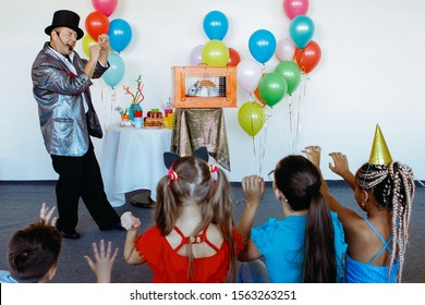 At a children's party, a magician, an illusionist shows tricks to a group of children in caps and with balloons. - Powered by Shutterstock