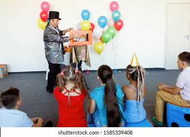 At a children's party, a magician, an illusionist shows tricks to a group of children in caps and with balloons. - Powered by Shutterstock