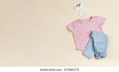 Children's Pink T-shirt, Folded Jeans And Elastic Band For Hair On A Beige Background. Copy Space.