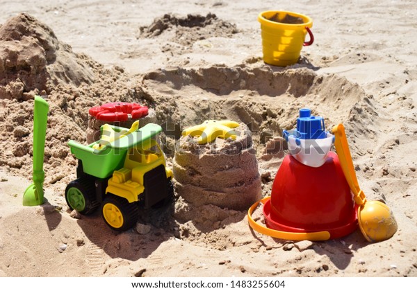 Children\'s plastic toys green end yellow car,\
shovel, yellow and red buckets, green ball with yellow sand on the\
beach by sea. Children\'s beach toys on sand on a sunny day. Sandbox\
on the playground