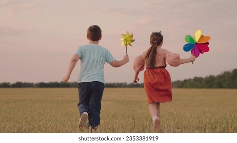 Childrens play pinwheel in nature. Happy children play with toy pinwheel outdoors in summer on field, running in park. Boy girl play together, wind turns circle toy. Family vacation in nature. Kid fly - Powered by Shutterstock