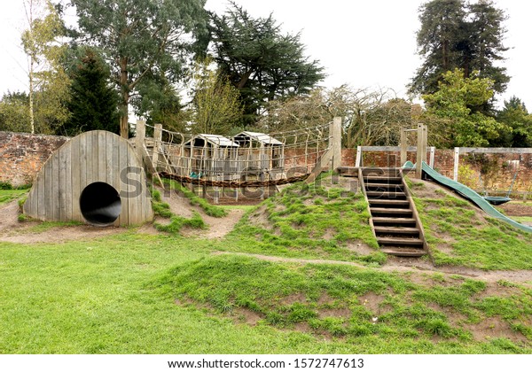 A childrens playground\
constructed using natural materials including wood and rope. A\
tunnel and slide built into the earth are connected by a climbing\
bridge. 