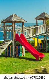 Children's playground on the beach. Red hill and wooden houses for children on green grass.