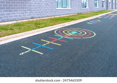 A children's' playground ring toss game painted on black pavement. There are yellow, red and green color circles and lines drawn on the ground. The activity is next to a grey brick school building. - Powered by Shutterstock