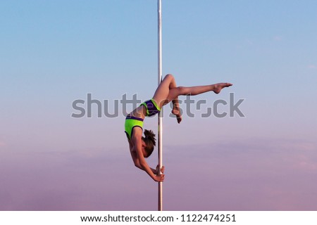 Children's Pole dance, kids aerial acrobatics on the sky background. A little girl performs tricks on the pylon in nature in the summer at sunset.
