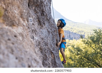 Children's rock climbing. The boy climbs a rock against the backdrop of mountains. Extreme hobby. An athletic child trains to be strong. Climbing safety. - Powered by Shutterstock