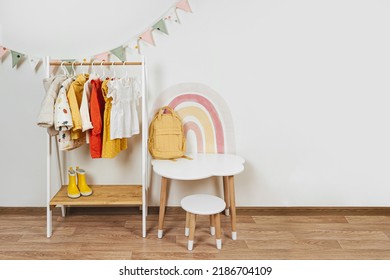 Children's room with Montessori Clothing Rack, white table and rainbow. Dress, jacket and sweaters on hangers in wardrobe. Nursery Storage Ideas. Montessori Toddler Room