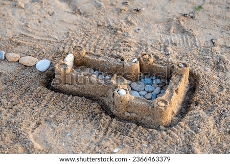 Children's sand castle on beach. Summer vacation. Sea stones and shells in sand.