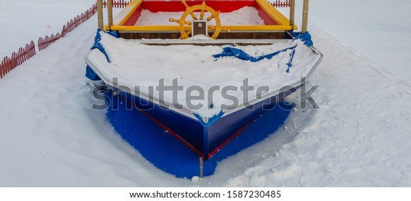 Children\'s sandbox in the form of a boat in winter\
under the snow.