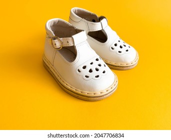 Children's Shoes, The Concept Of The First Step. Baby White On A Yellow Colorful Background. Space For The Text. The First Steps Of The Baby. Children's Background. Orthopedics. Top View, Layout
