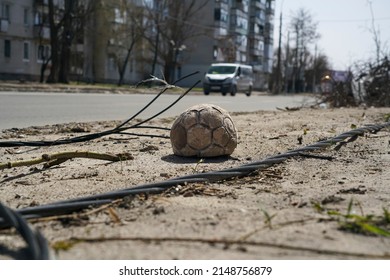 A children's soccer ball lies near the road against a building destroyed by an explosion in the war in Ukraine. Nearby are the wires of a broken power line.