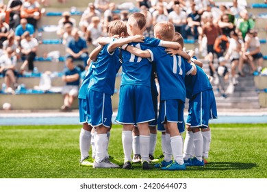 Children's sports team. Kids play sports match on the stadium field. School boys in blue jersey shirts huddling in a team. Parents sitting at the stadium and watching pupils in the background  - Powered by Shutterstock