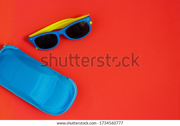 children\'s sunglasses with colored frames and\
a blue case for glasses in the shape of a car on a red background.\
Summer holiday concept,\
minimalism
