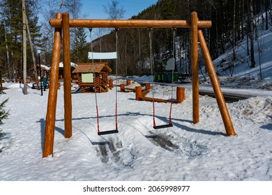 Childrens Swing In The Winter In The National Park. Hanging Swing On Wooden Supports. Swing On The Playground In Winter.