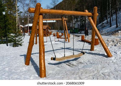 Childrens Swing In The Winter In The National Park. Hanging Swing On Wooden Supports. Swing On The Playground In Winter.