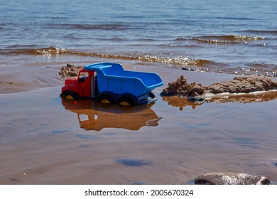 Children's toy bright blue plastic dump truck on the sandy beach of the sea . High quality photo