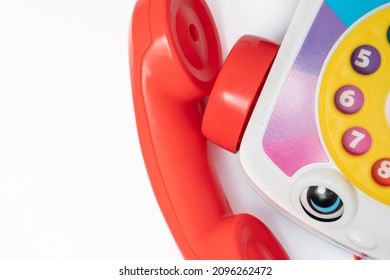 Children's toy landline phone with a red receiver, a dial and a smile on the body isolated on white