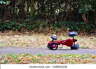 A Children's Toy Tricycle Bike Tractor Left Tipped Over Abandoned On A Path In A Kids Play Park On A Farm.