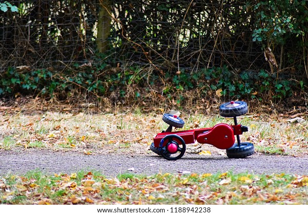 A children\'s toy\
tricycle bike tractor left tipped over abandoned on a path in a\
kids play park on a farm.