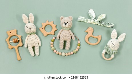 Children's toys on a green mint background. Wooden and knitted baby handmade toys in eco style for a banner. Infant baby toys concept. Wooden rattles, crocketed teddy bear and teething beads top view.