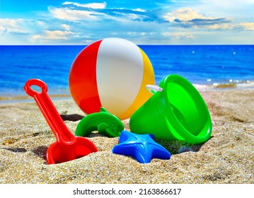 Children's toys for playing in the sandbox on the beach sand against the background of the sea and cloudy sky on a sunny day - Powered by Shutterstock