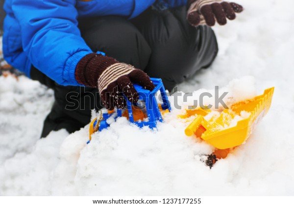 Children\'s\
winter games outdoors. The image of the child , who sits on the\
white snow and playing with a toy\
excavator.