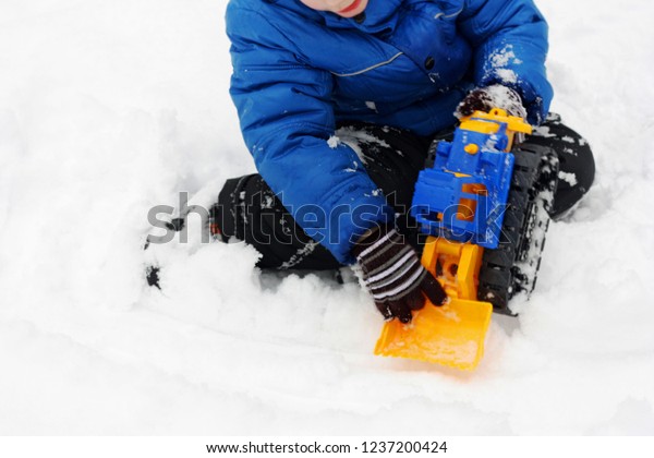 Children\'s\
winter games outdoors. The image of the child , who sits on the\
white snow and playing with a toy\
excavator.