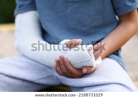a child's arm is broken. little boy with a fractured limb outdoors. fracture injury in the summer holiday. kid is moving fingers in plaster cast on the arm