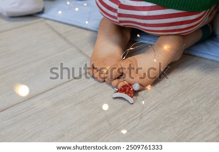 child's bare feet on the floor, a garland, a small decorative Santi hat. selective focus. Cozy homely holiday atmosphere. Waiting for a miracle, a fairy tale at home